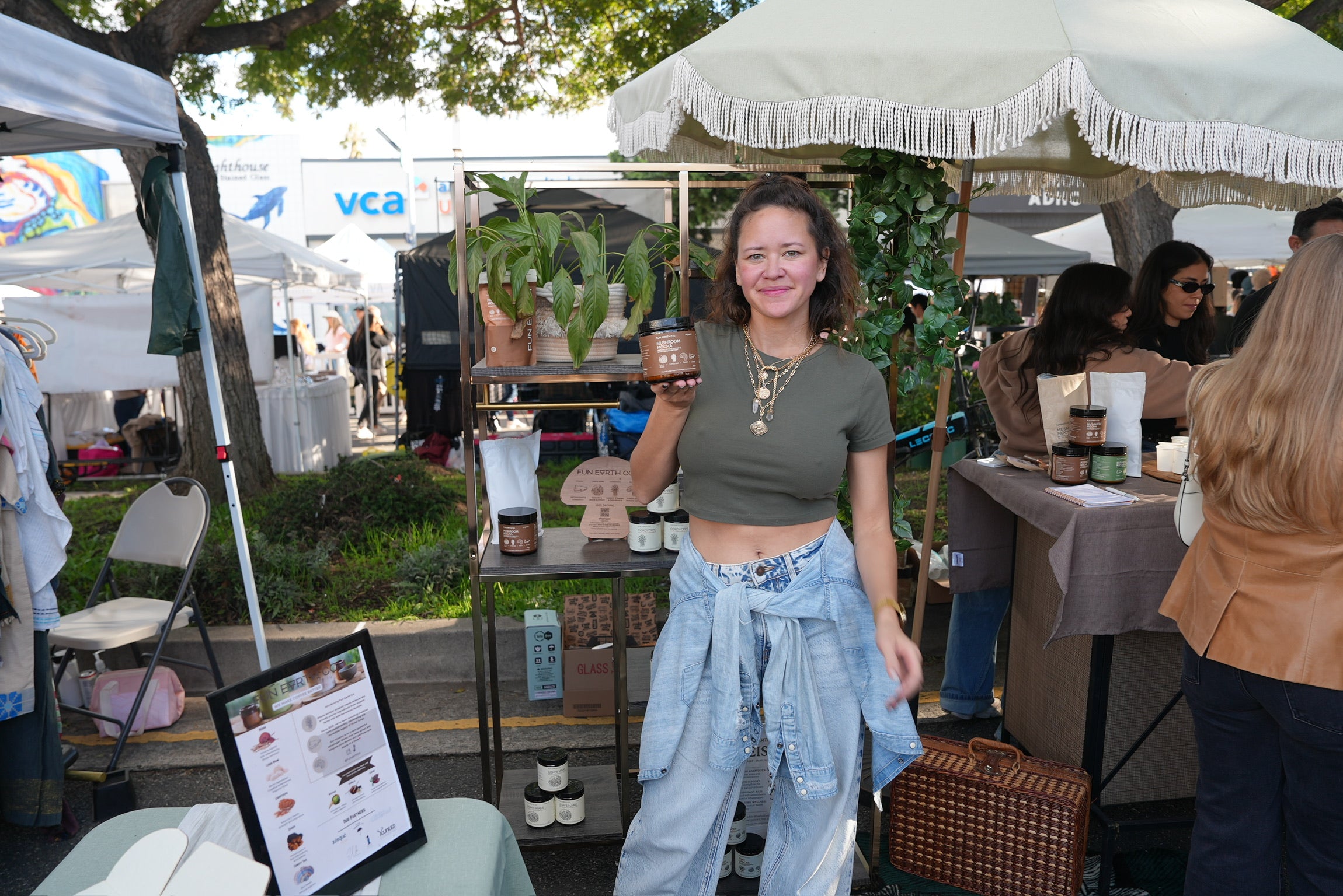 Two people holding Fun Earth Mushroom Mocha and Mushroom Matcha Latte jars at a community market
